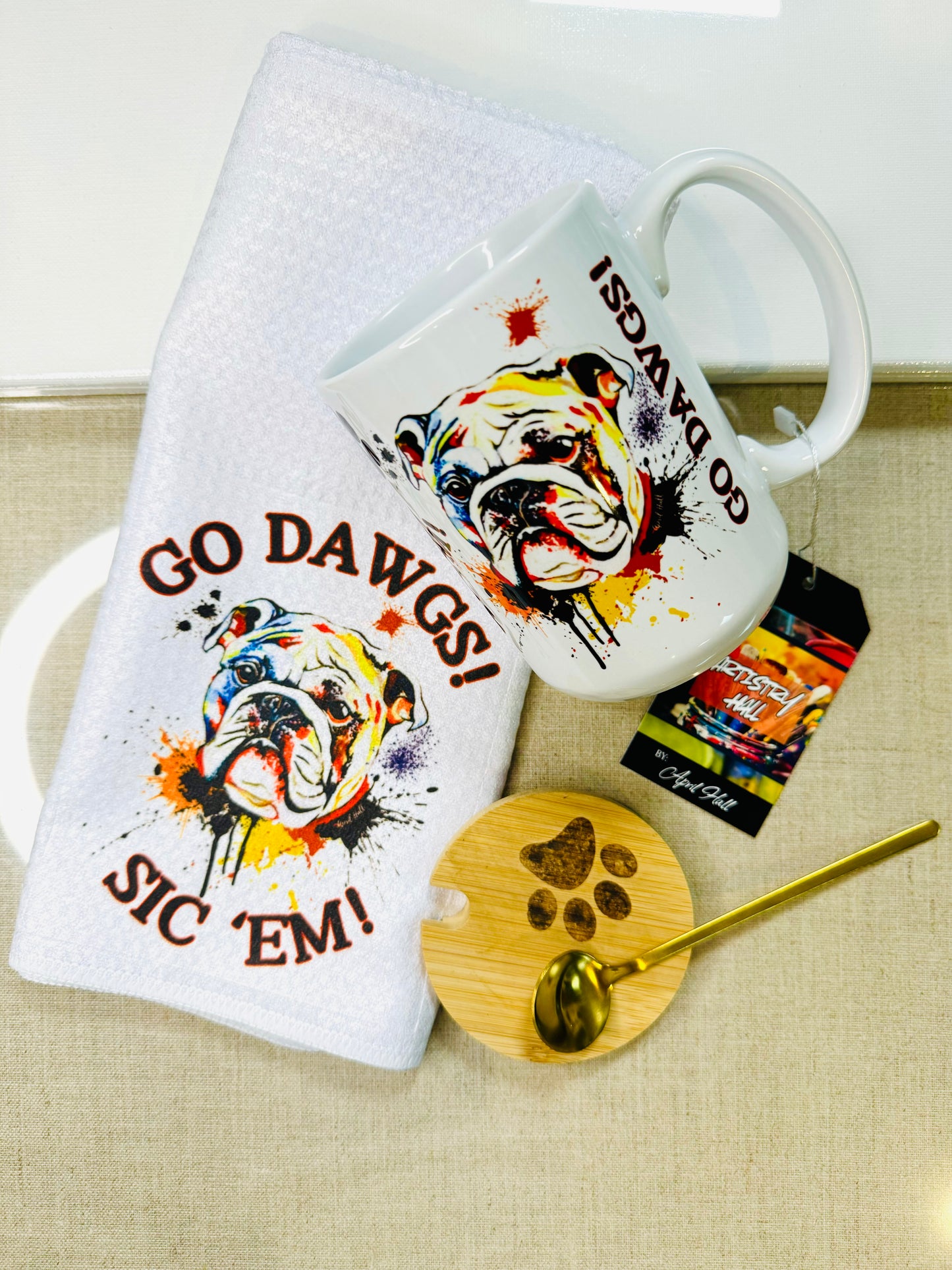 A set of Go Dawgs themed kitchenware and accessories, including a white tea towel with bulldog, a multicolor wine tumbler, coffee cup, and a circle leather keychain.