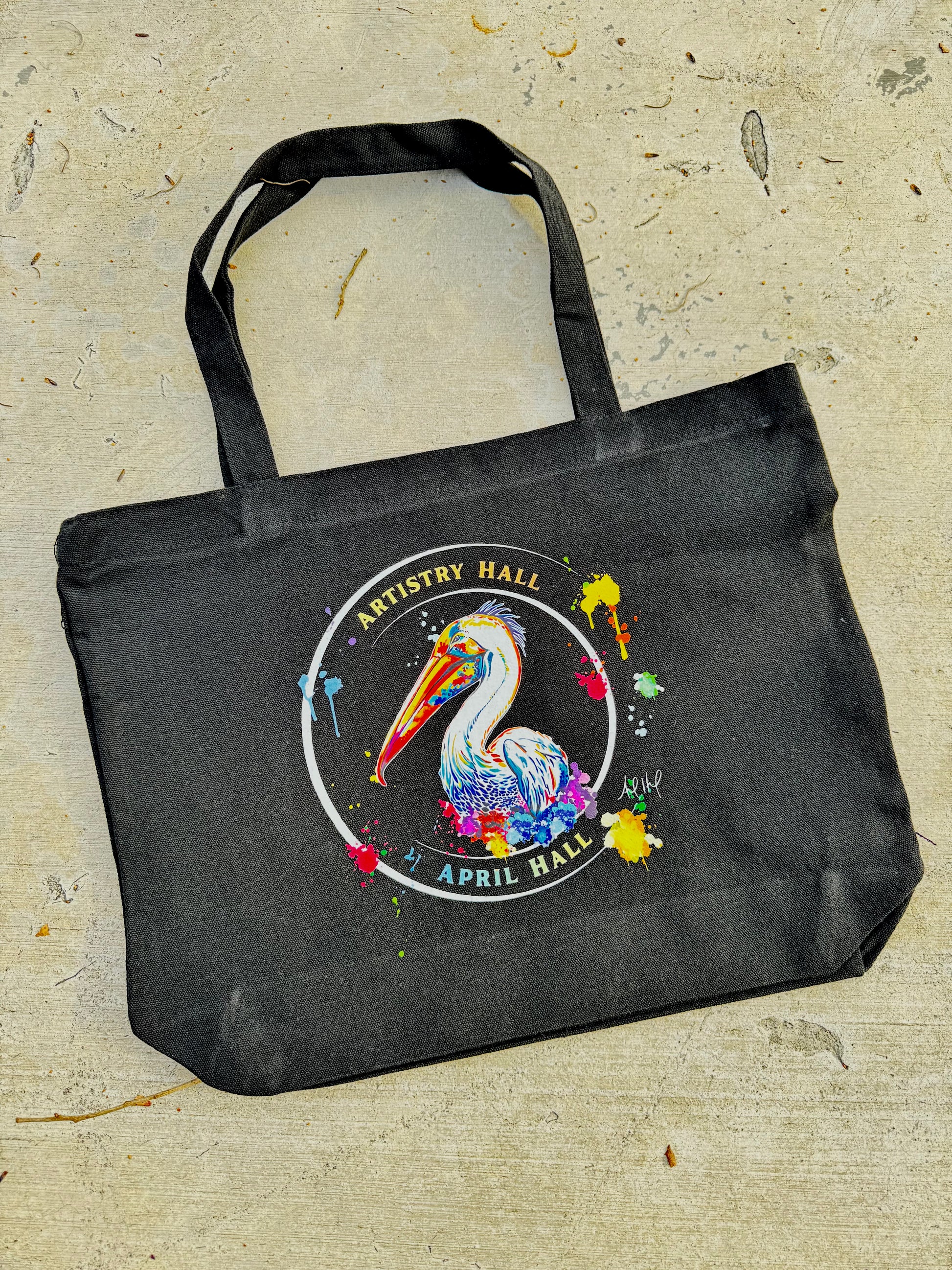 Black tote bag with Pelican design with the name "Artistry Hall" & artist "April Hall"
